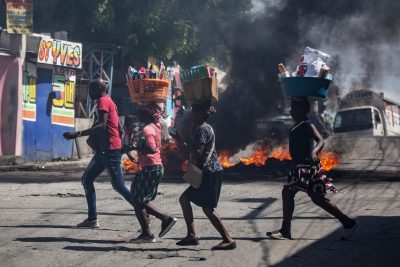 Personas corren con algunas pertenencias durante una protesta este lunes, en el barrio Solino en Puerto Principe (Haití).